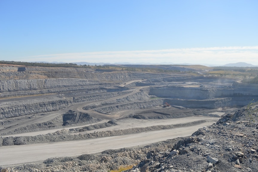An open cut coal mine with high grey walls surrounded by farmland