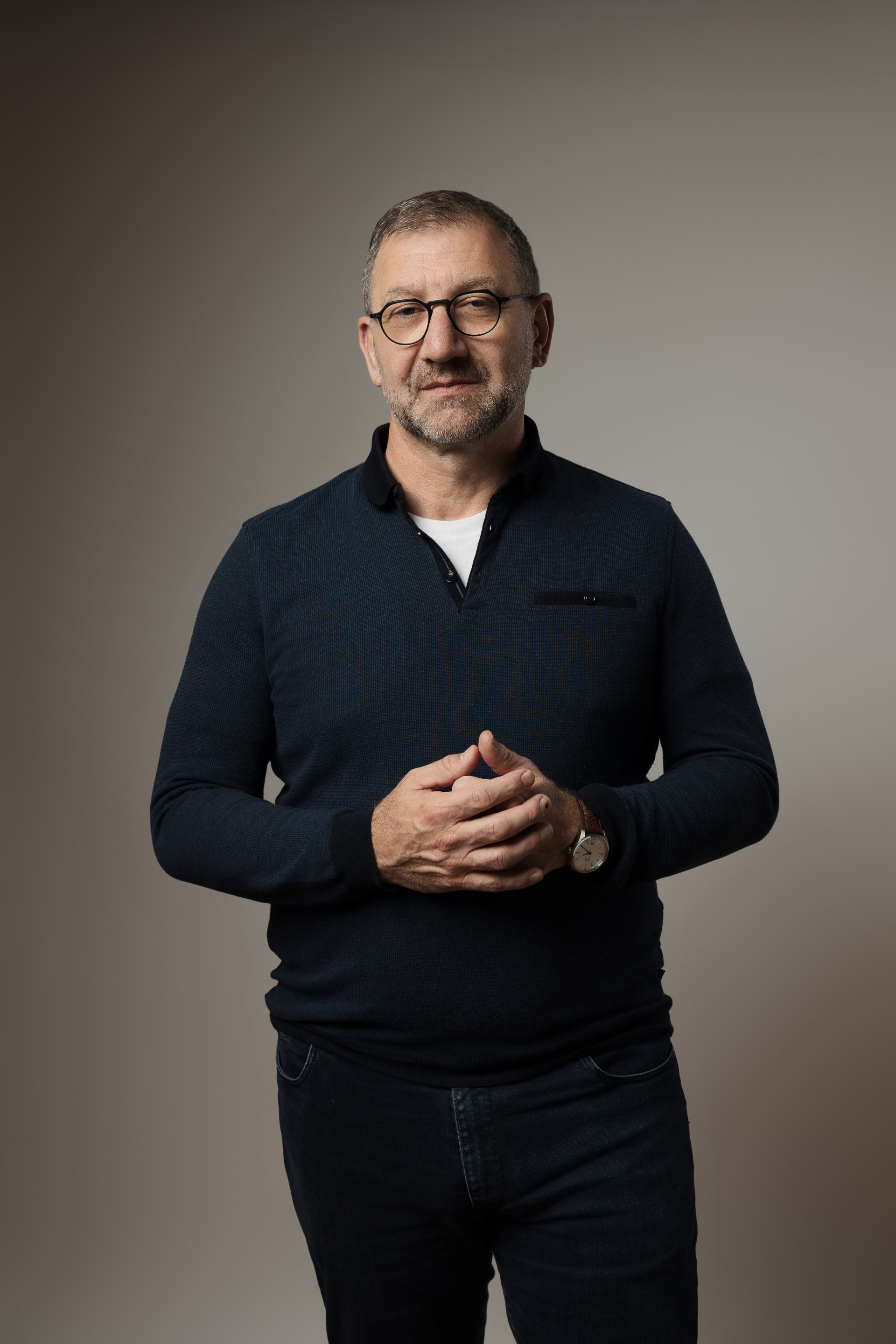 A man wearing glasses has a serious expression strewn on his face for his work portrait.