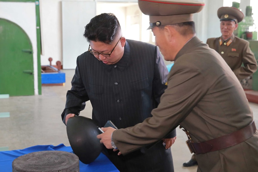 Kim Jong-un is shown a piece of black equipment by an officer.