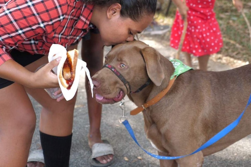 Young Indigenous woman plants a kiss on the top of a dog's head