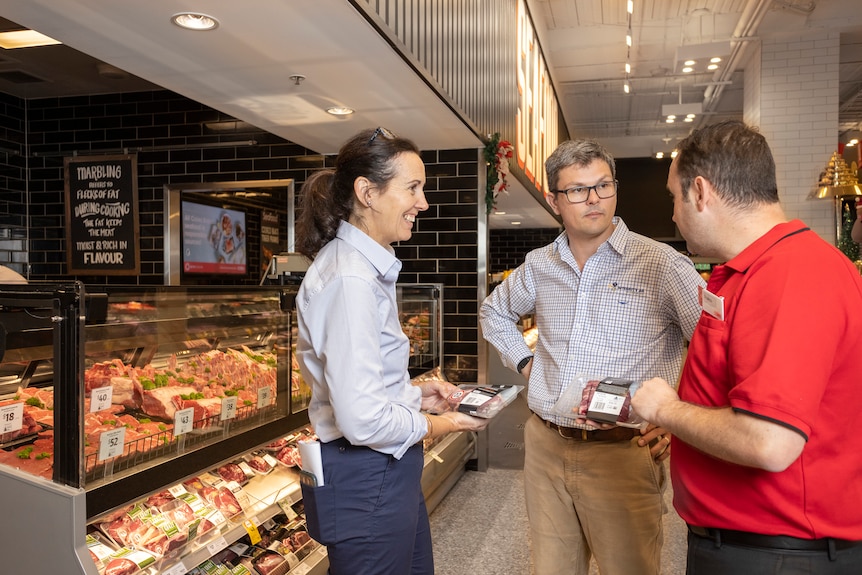 A woman stands next to two men in a supermarket as they hold carbon neutral beef
