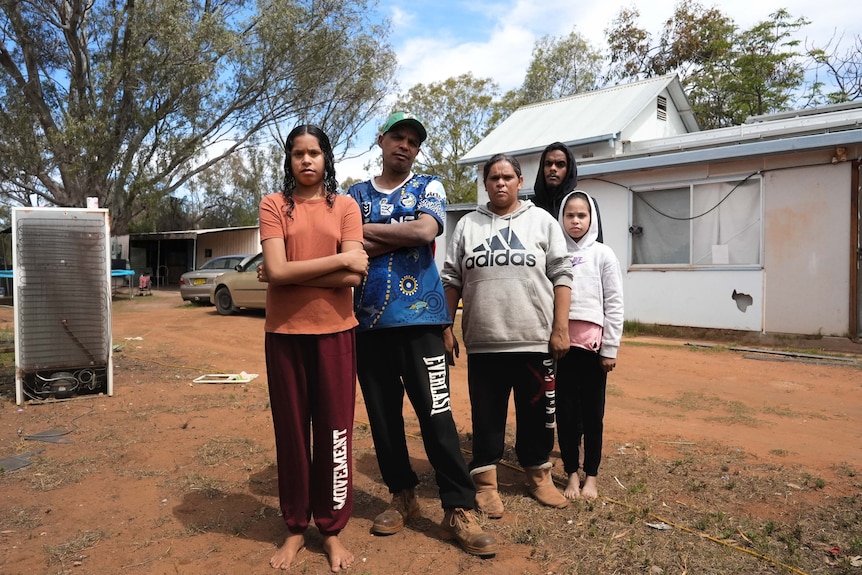 A family of five stands in front of a house.