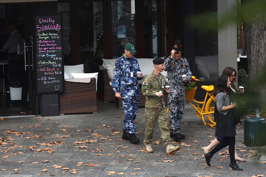 Three men in different coloured military uniforms purchase takeaway coffees from an East Perth cafe.