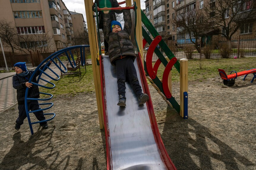 A boy sliding in a playground, with another child in the background.