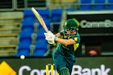 A medium shot of a female cricketer with a helmet on holding up their bat while striking a ball during a match.