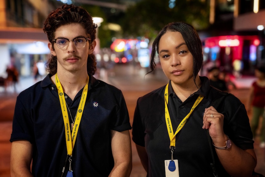Two young people in black polos stand on a busy city street. 