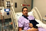 Injured cyclist Peter Duncan sits in a hospital bed with an arm in a sling.