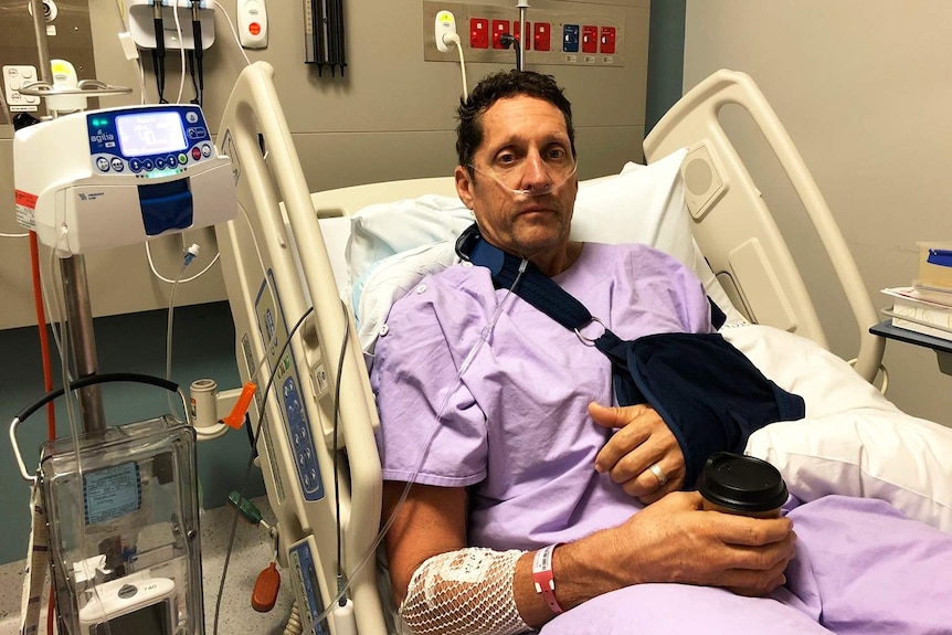 Injured cyclist Peter Duncan sits in a hospital bed with an arm in a sling.