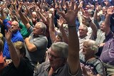 A crowd of 500 seated people with their hands raised