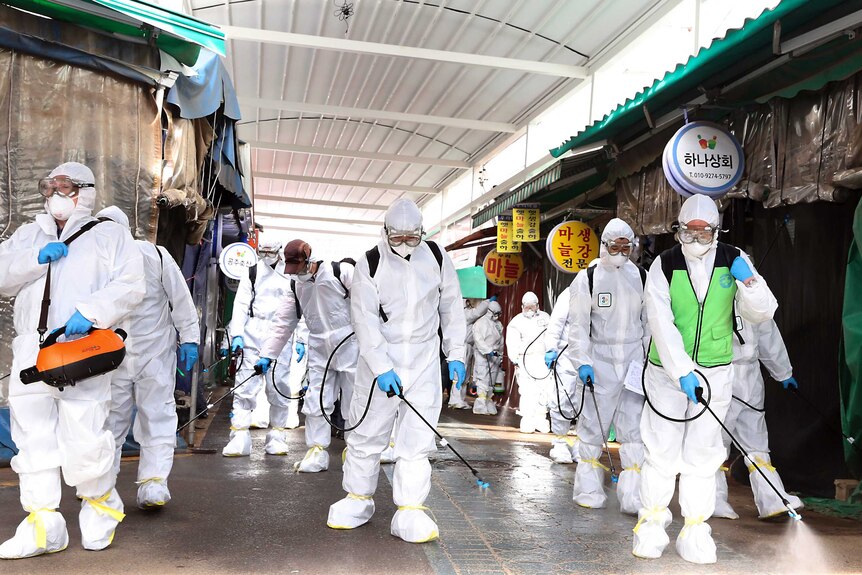 Workers wearing protective suits spray disinfectant through a closed market place.