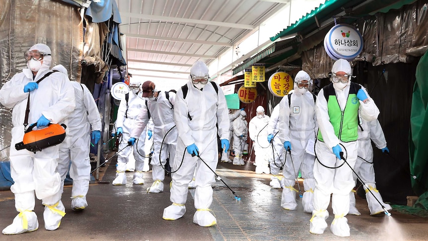 Workers wearing protective suits spray disinfectant through a closed market place.