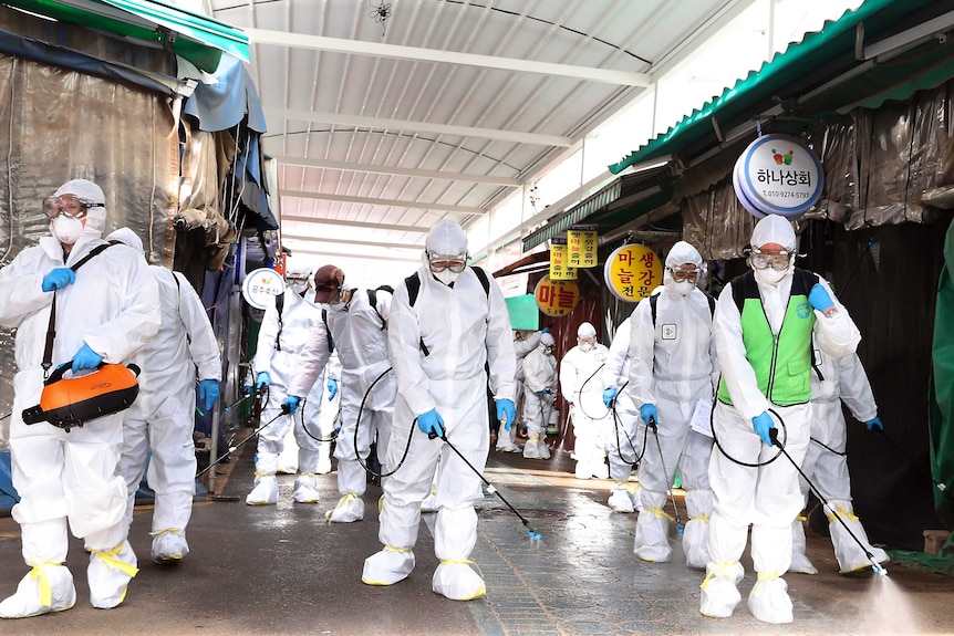 Workers wearing protective suits spray disinfectant through a closed market place.