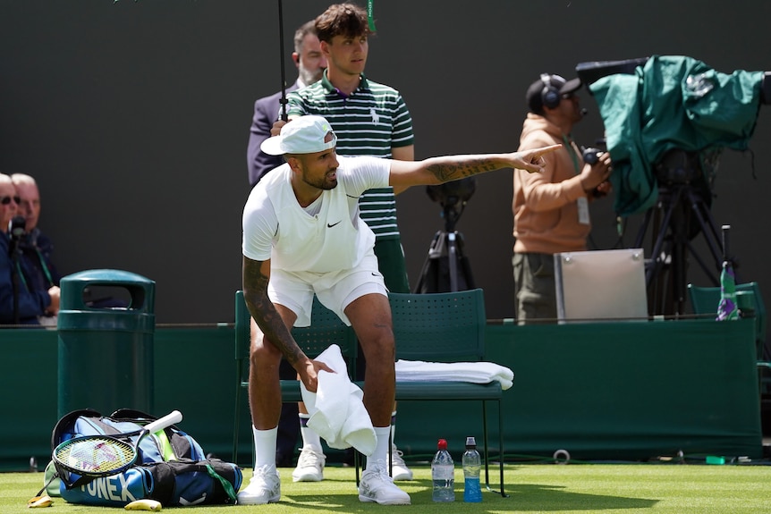 Nick Kyrgios points to one side as he sits on a chair