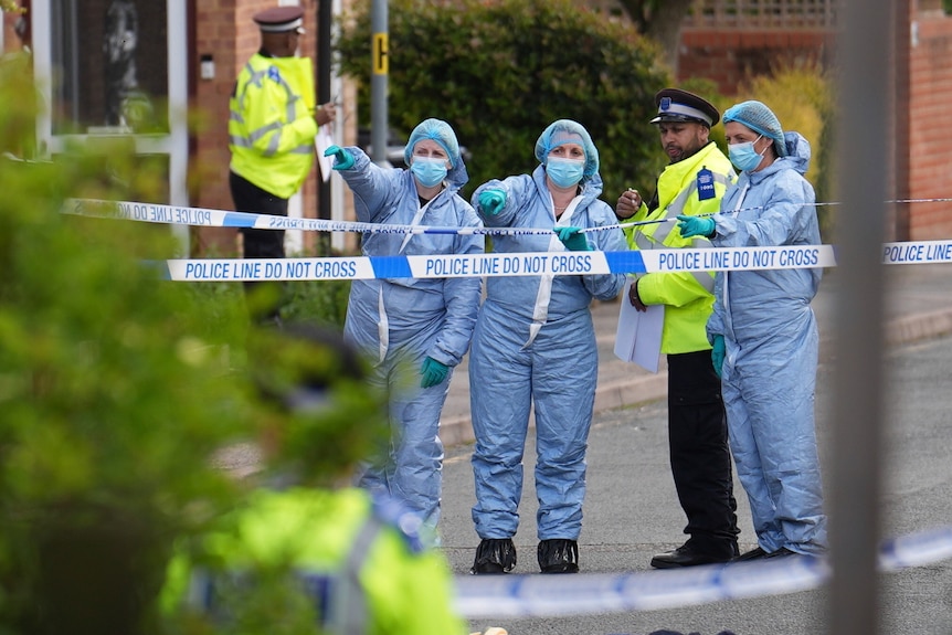 Three people in blue and white surgeon's gear stand next to a police officer in hi-vis.