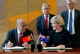 Agio Pereira and Julie Bishop sign paperwork in front of small East Timor and Australian flags.