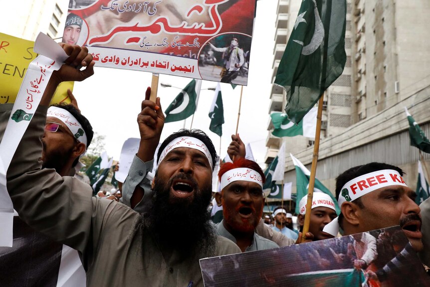 Men in Pakistan shouting and marching down a street holding Pakistani flags