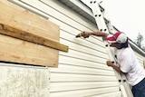 A man reinforces drills boards over windows as he reinforces his mobile home.