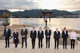 G7 leaders line up for photo call by the seaside, with a Japanese mon (gate) seen in the water behind.