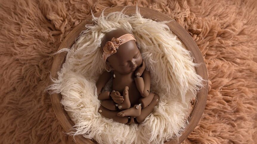 A baby mannequin laying on two layers of shag carpet in pinks and whites.