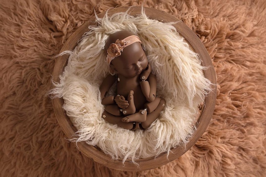 A baby mannequin laying on two layers of shag carpet in pinks and whites.