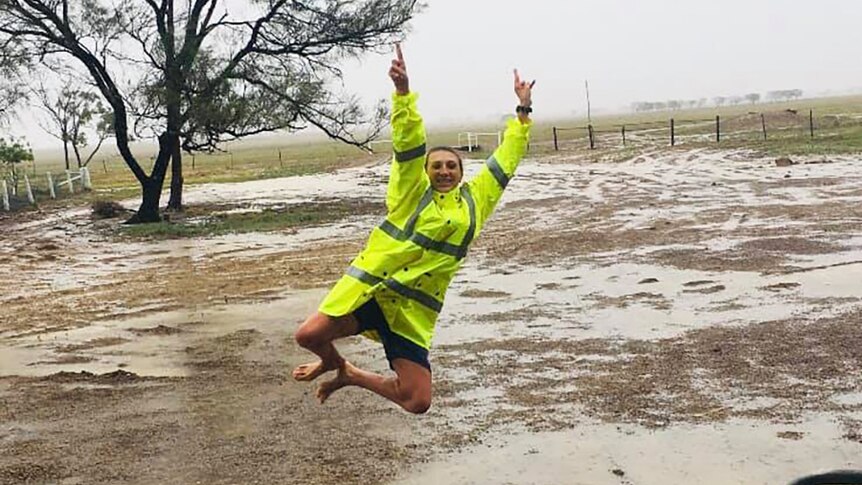 A woman leaps for joy to see rain falling on her outback property