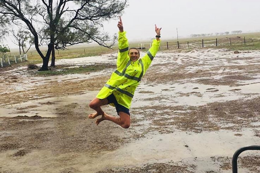 A woman leaps for joy to see rain falling on her outback property