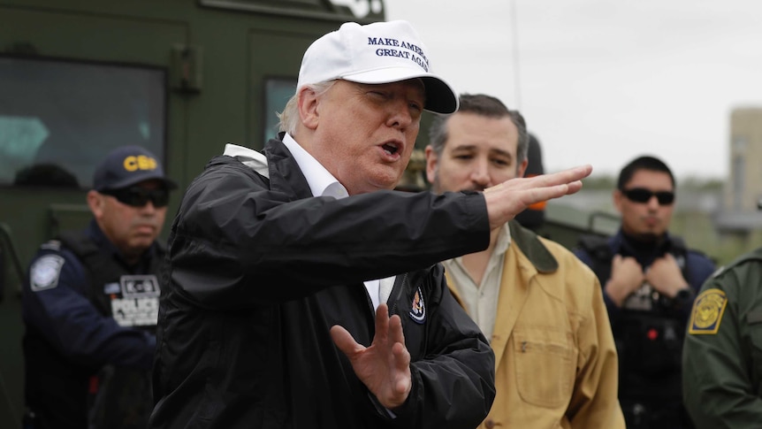 Trump wearing a white Make America Great Again cap gesturing in front of Ted Cruz and border patrol troops.