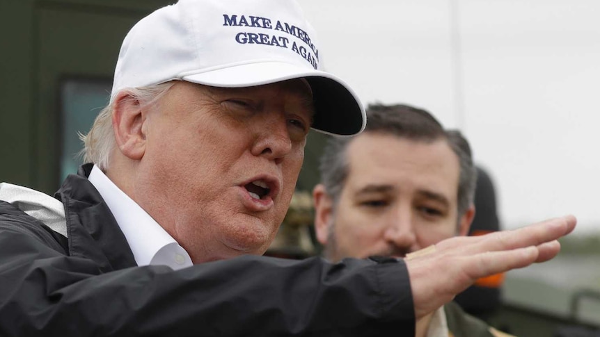 Trump wearing a white Make America Great Again cap gesturing in front of Ted Cruz and border patrol troops.