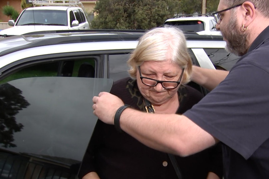 A man holds a car door open as a woman gets out.