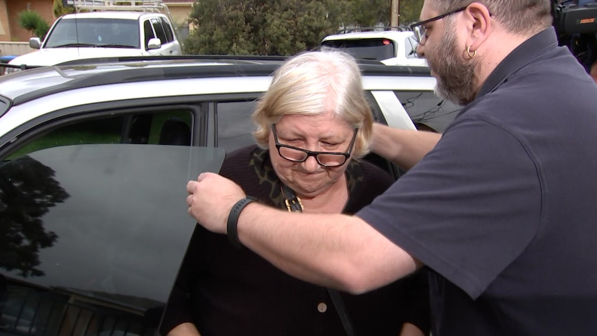 A man holds a car door open as a woman gets out.