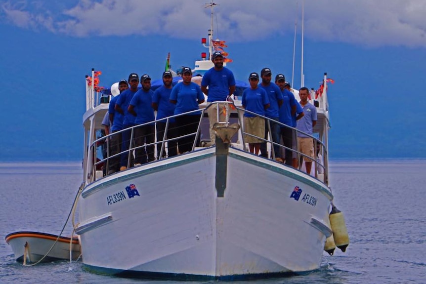 A boat with people standing on the deck posing for a photo.