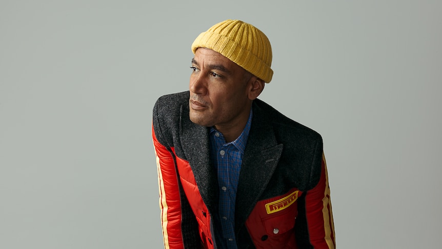 Ben Harper wears a yellow hat and a red racing jacket. He stares into the distance