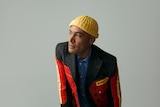 Ben Harper wears a yellow hat and a red racing jacket. He stares into the distance