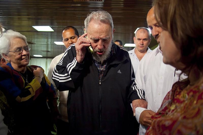 Surrounded by people, Fidel Castro speaks on a mobile phone while clutching the arm of a man next to him