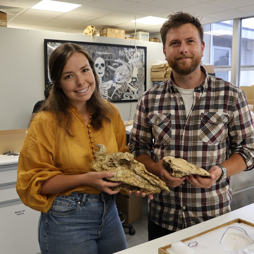 A woman and a man stand in a lab with old giant bird bones in their hands