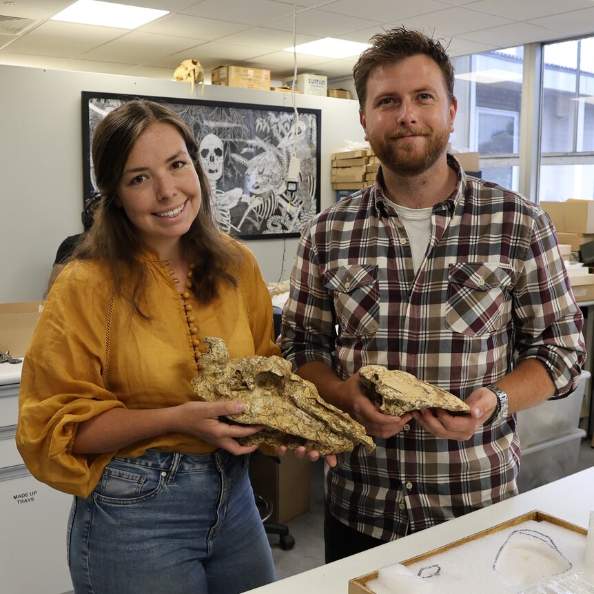 A woman and a man stand in a lab with old giant bird bones in their hands