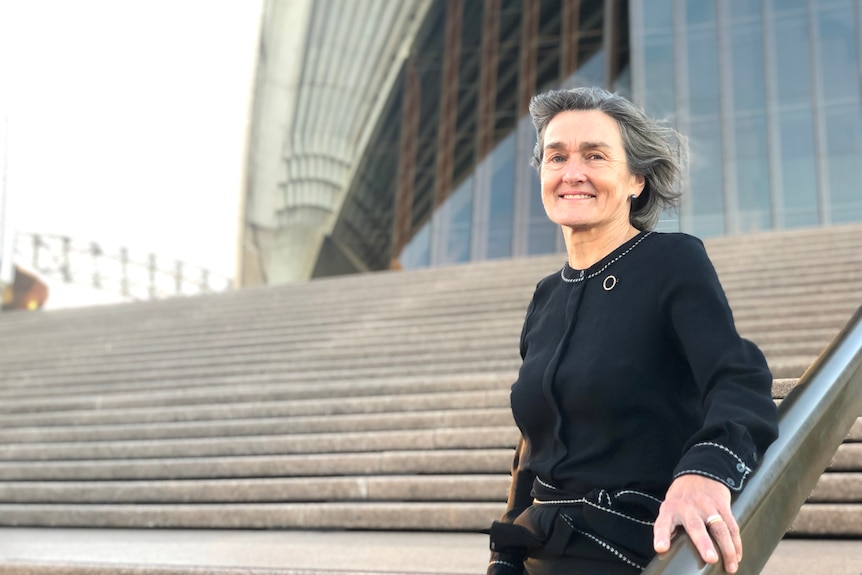 Louise Herron, wearing black, standing on the steps of the Sydney Opera House. 