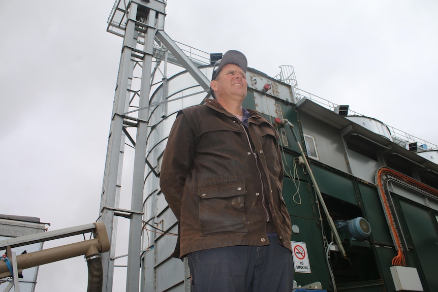 Man stands in front of large silos, looking off into distance