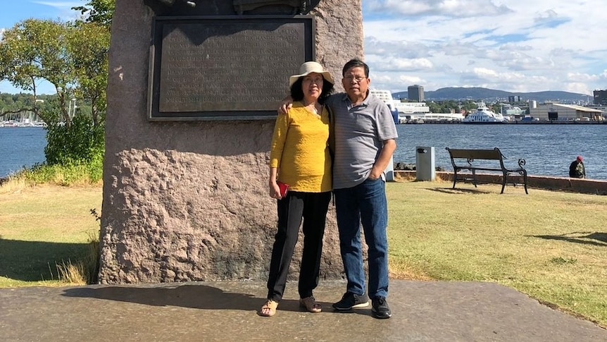 A man and a woman in a holiday snap in front of a statue.
