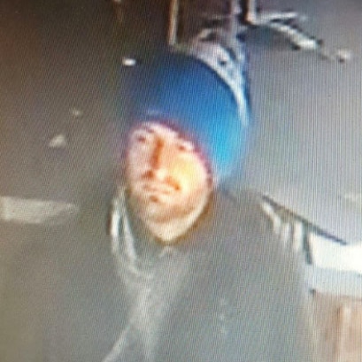 A man on CCTV wearing a blue beanie and dark coat.