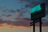 A large blue neon sign that reads 'HOTEL' pictured in front of a dusky sunset