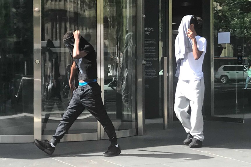 Two men walk with jackets over their heads.