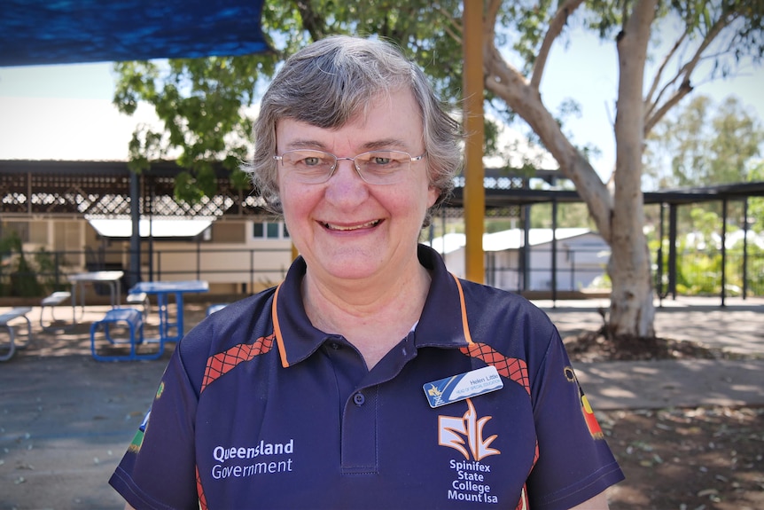 Woman with grey hair and glasses wearing purple shirt smiles at camera