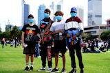 Four boys wearing face masks standing on lawn at Langley Park in front of Perth skyscrapers.