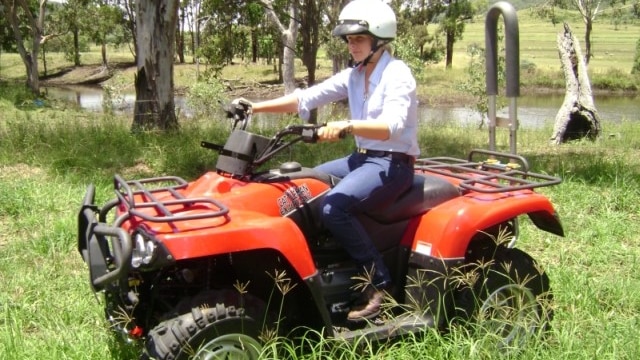 A young rider with a helmet on a quad bike with a roll bar.