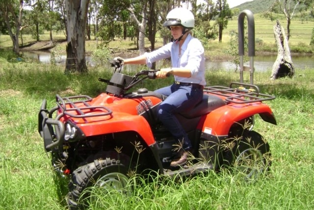 A young rider with a helmet on a quad bike with a roll bar.