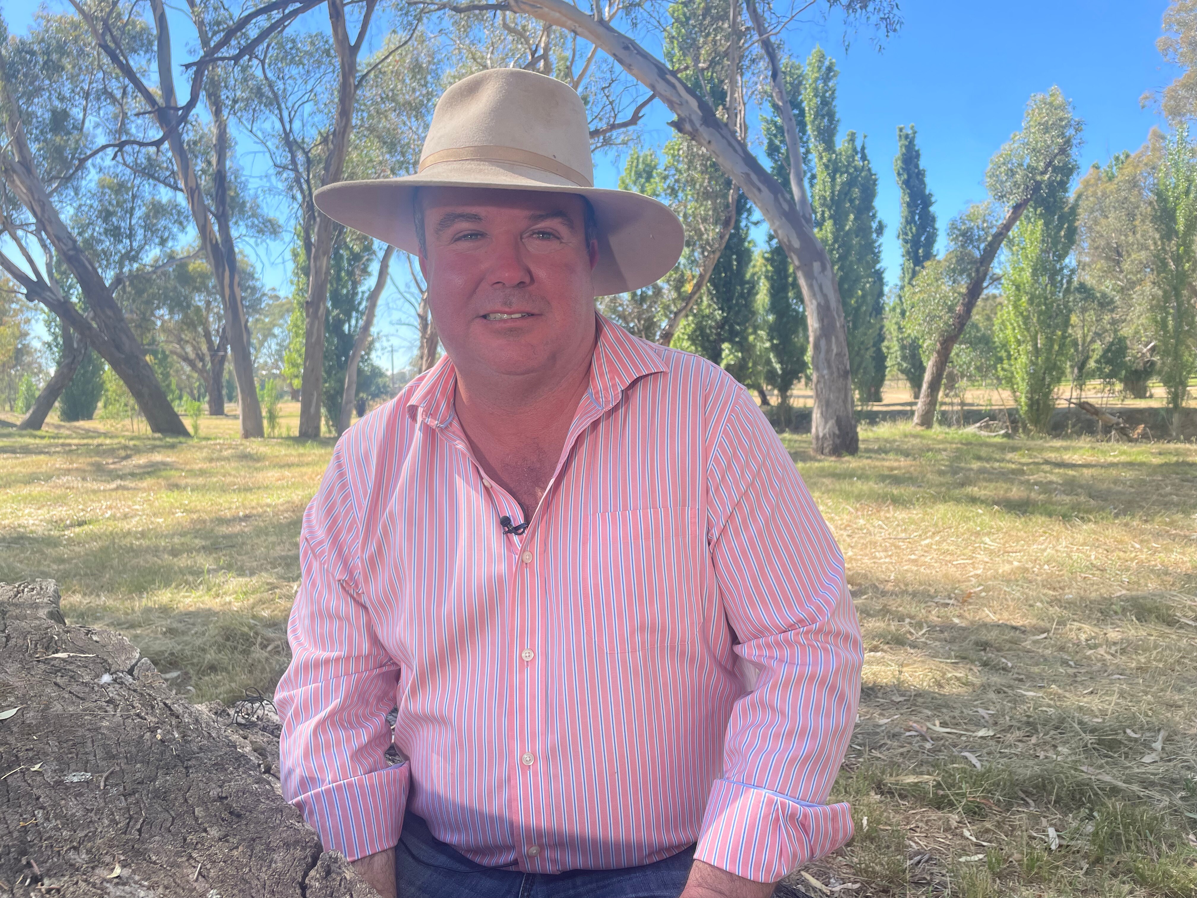 A man in a pink shirt and hat, sitting outdoors.