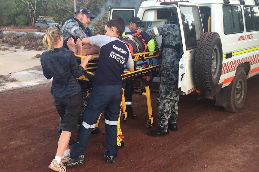 The injured yachtsman is placed in an ambulance by medical staff and navy personnel.