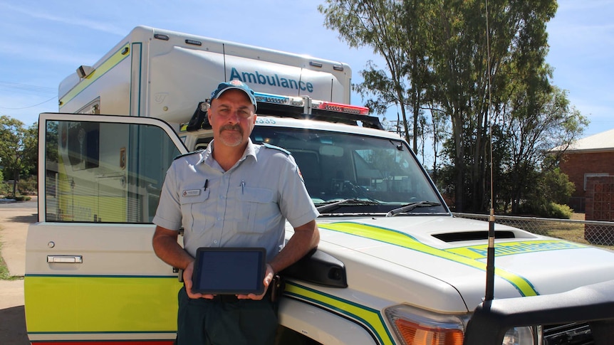 Officer in charge of Eidsvold ambulance station Scott Wicks stands in front of ambulance with his tablet.