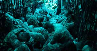US soldiers on C-130 sitting close heads down bathed in blue-green light